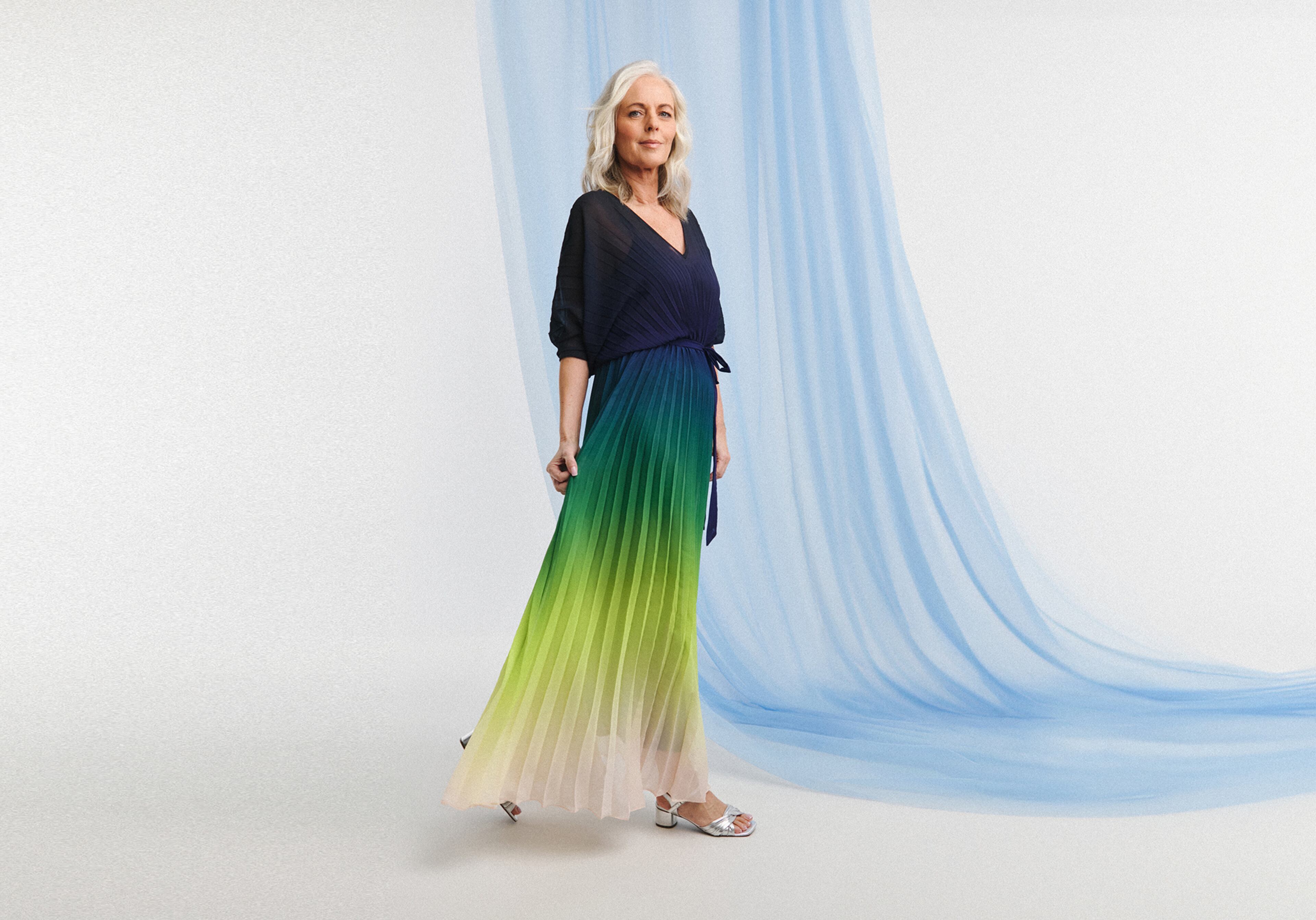 A woman stood, wearing a graduated green and blue skirt with navy blue blouse