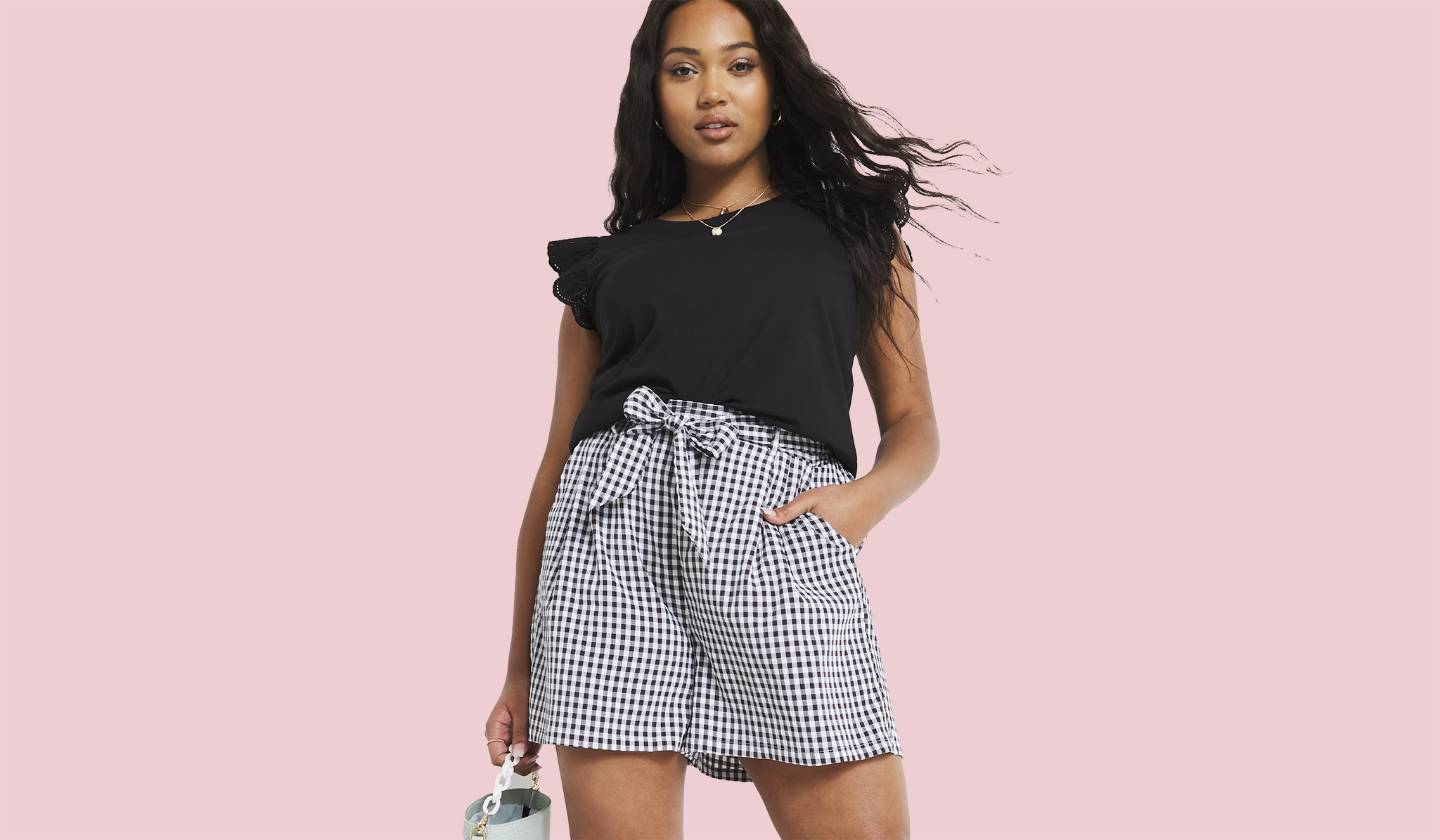 A woman stood wearing a frilly black sleeveless blouse with black and white checked shorts